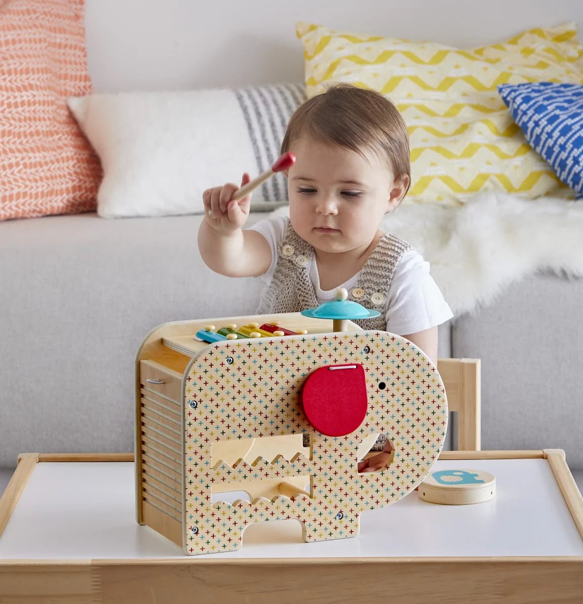 Child playing with a wooden toy on a table with colorful cushions in the background