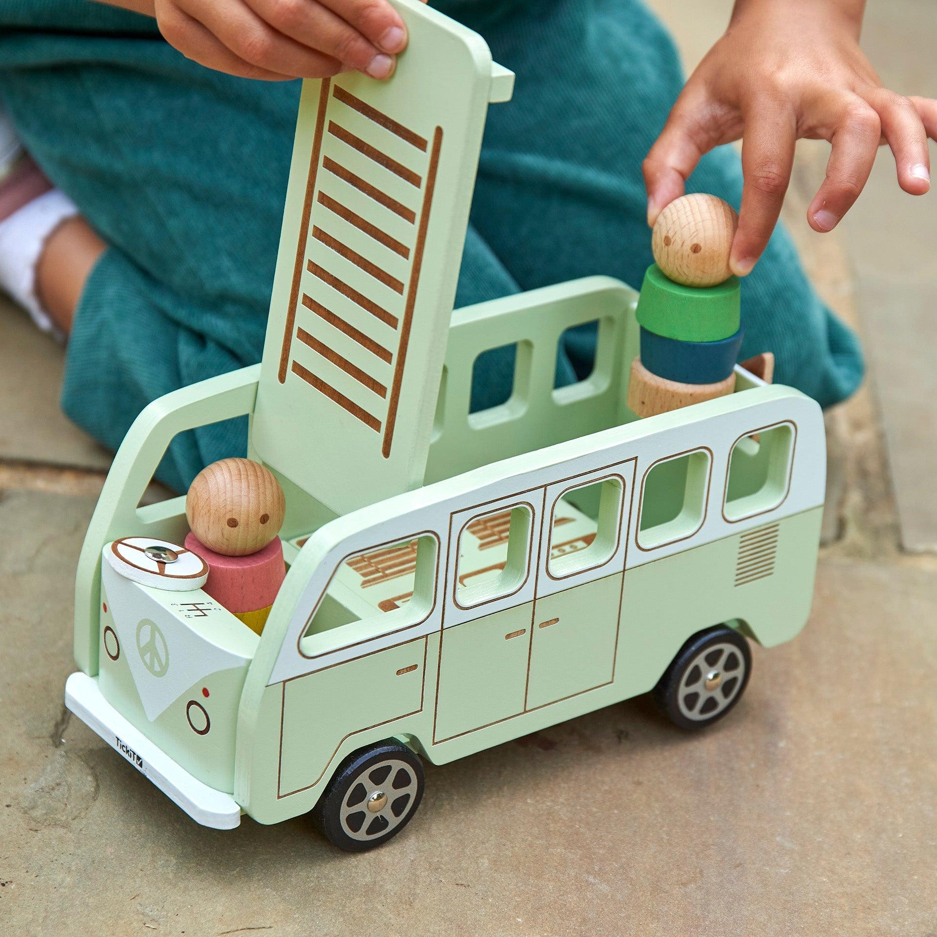 Children playing with a wooden toy van and figurines on a wooden floor.