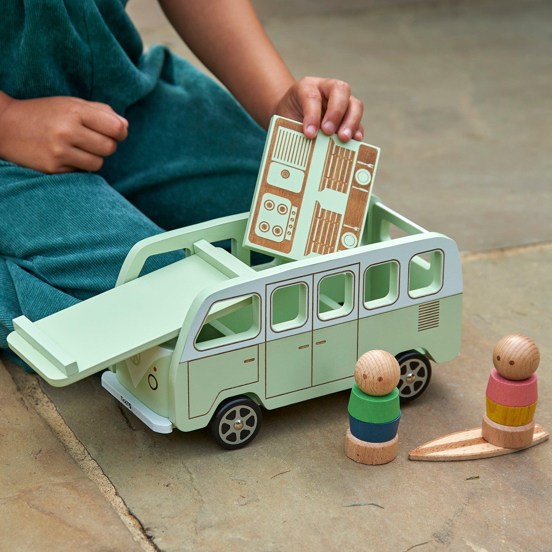 Child playing with a toy bus and wooden figures on a concrete surface