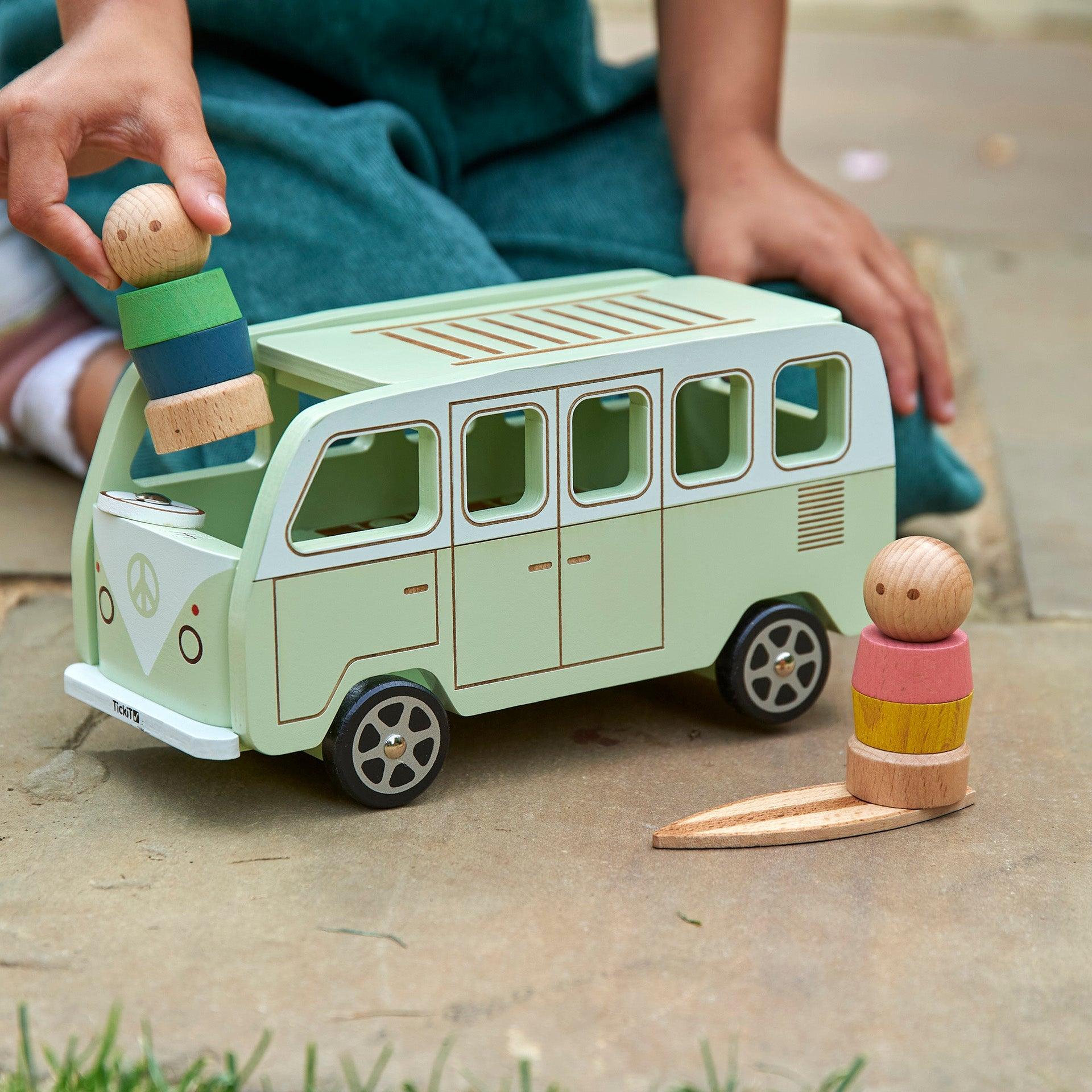 Child playing with a green toy van and wooden figures on a concrete surface.
