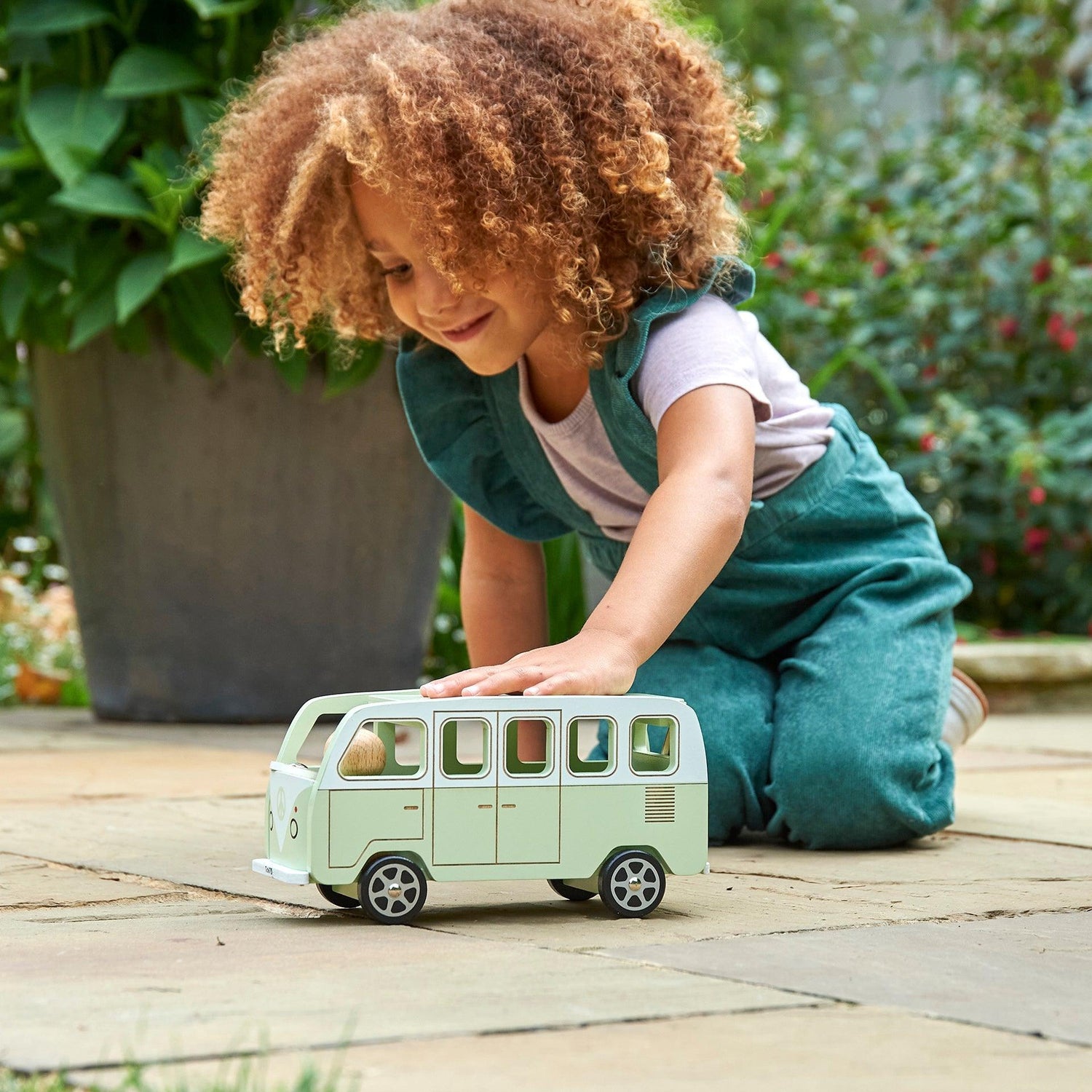 Child playing with a toy van outdoors on a wooden surface