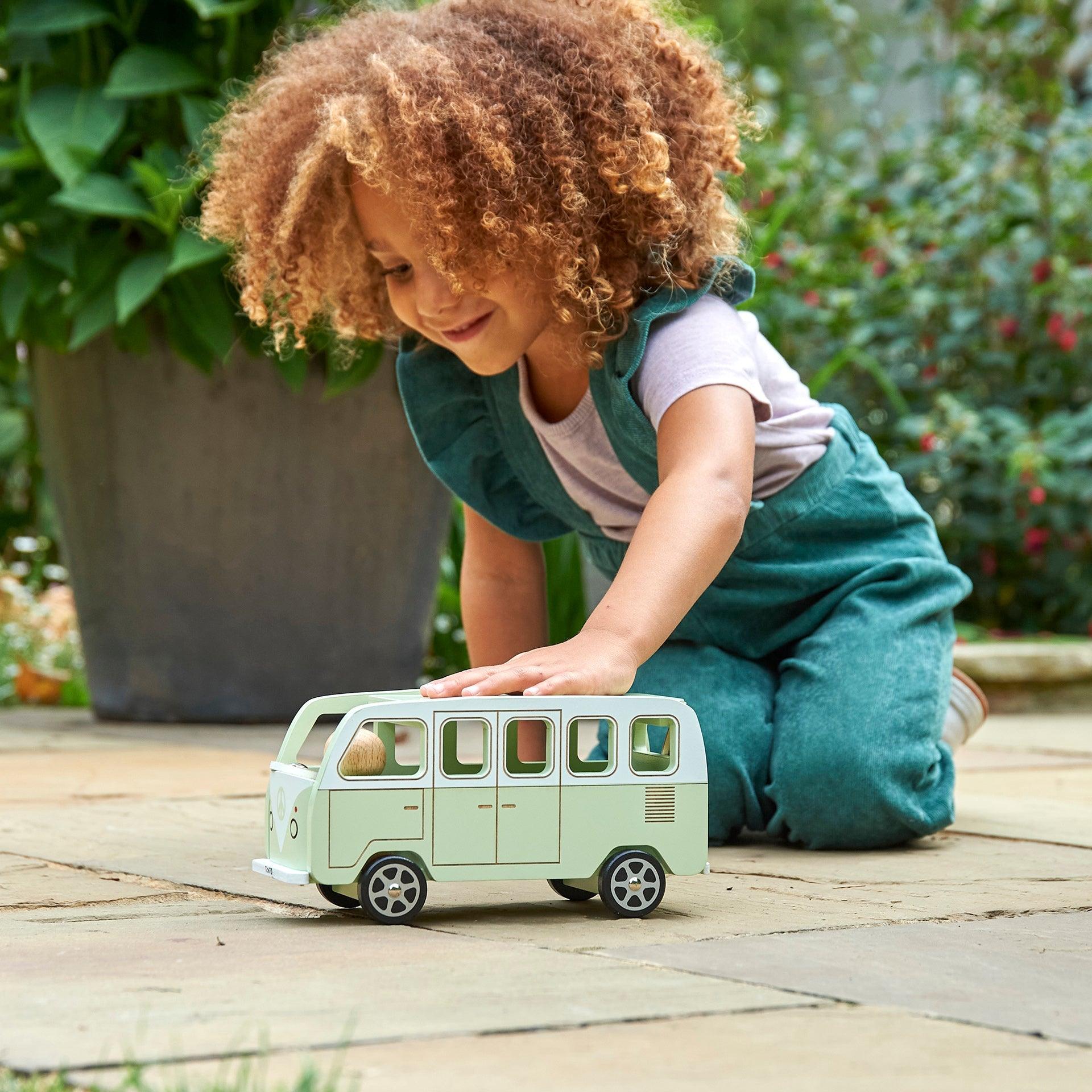 Child playing with a toy van outdoors on a wooden surface