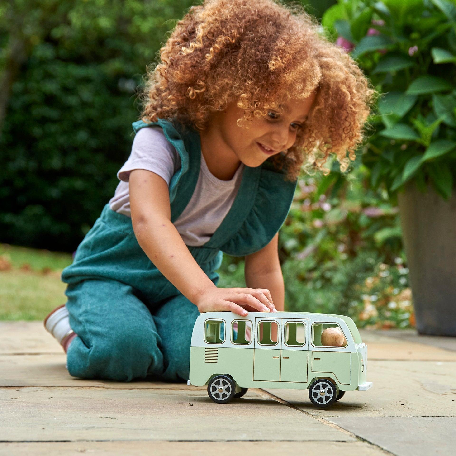 Child playing with a toy van outdoors on a wooden surface