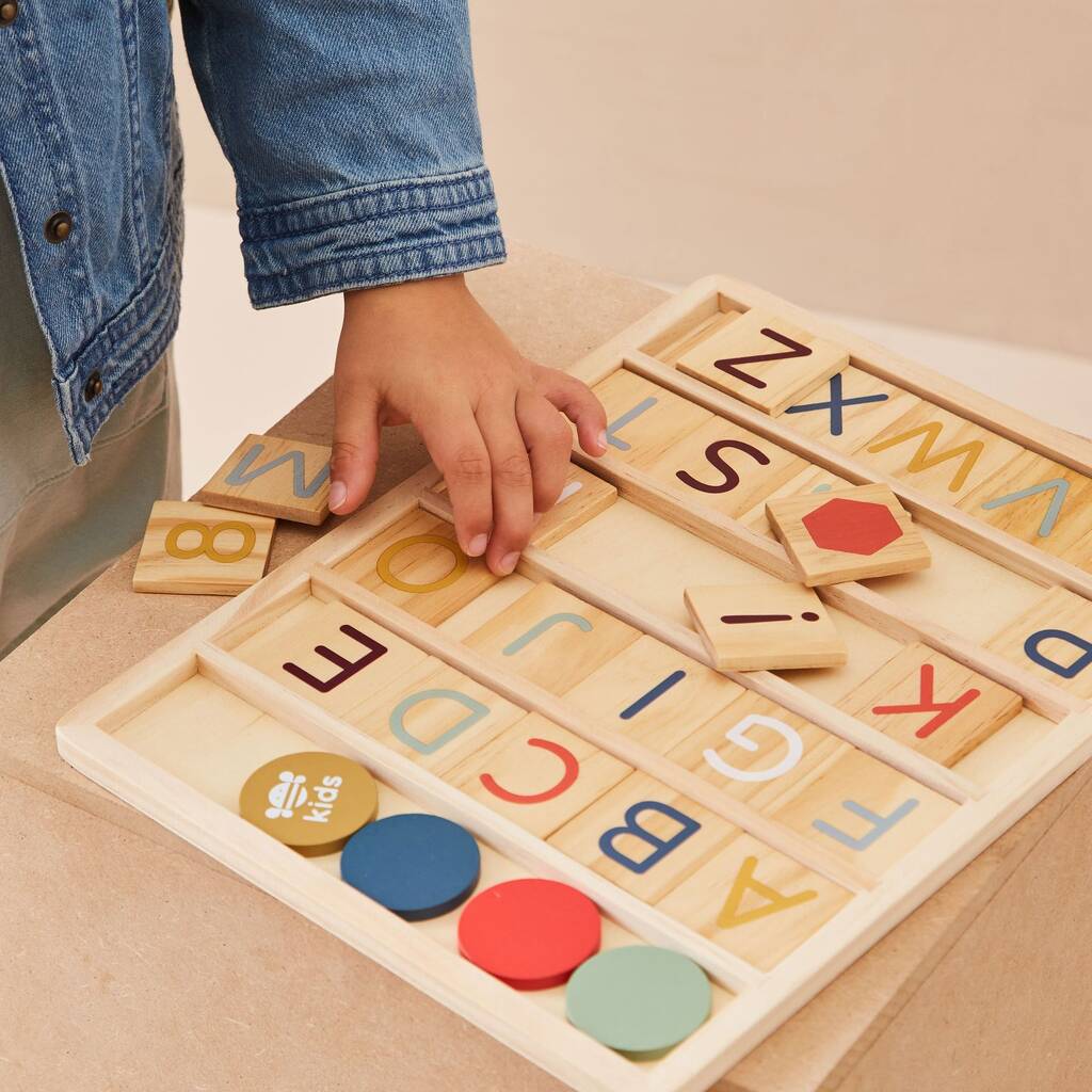 Child playing with a wooden alphabet and shape puzzle on a beige surface.
