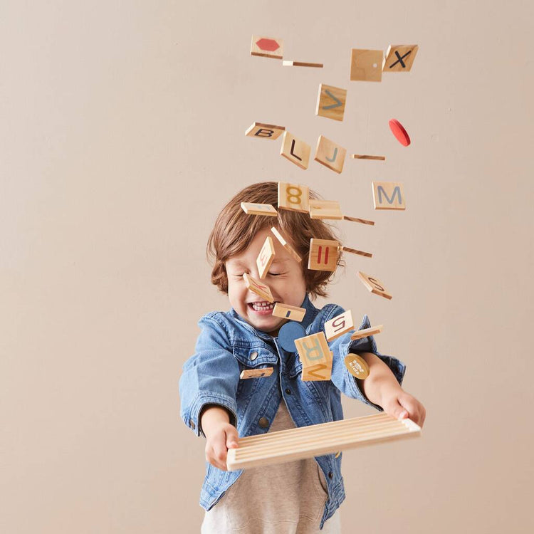 Child playing with wooden letters and blocks against a beige background