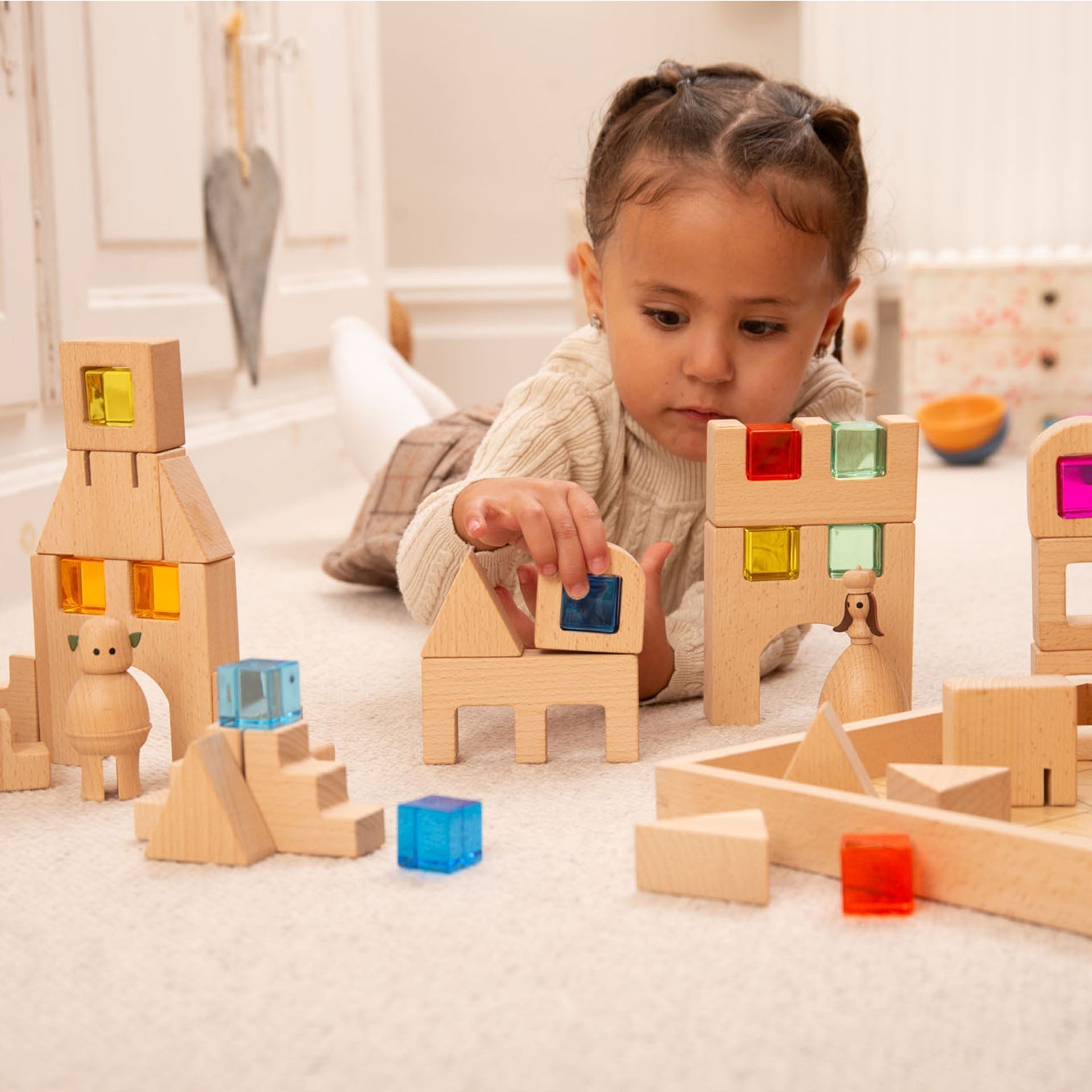Child playing with wooden building blocks on a light-colored floor.