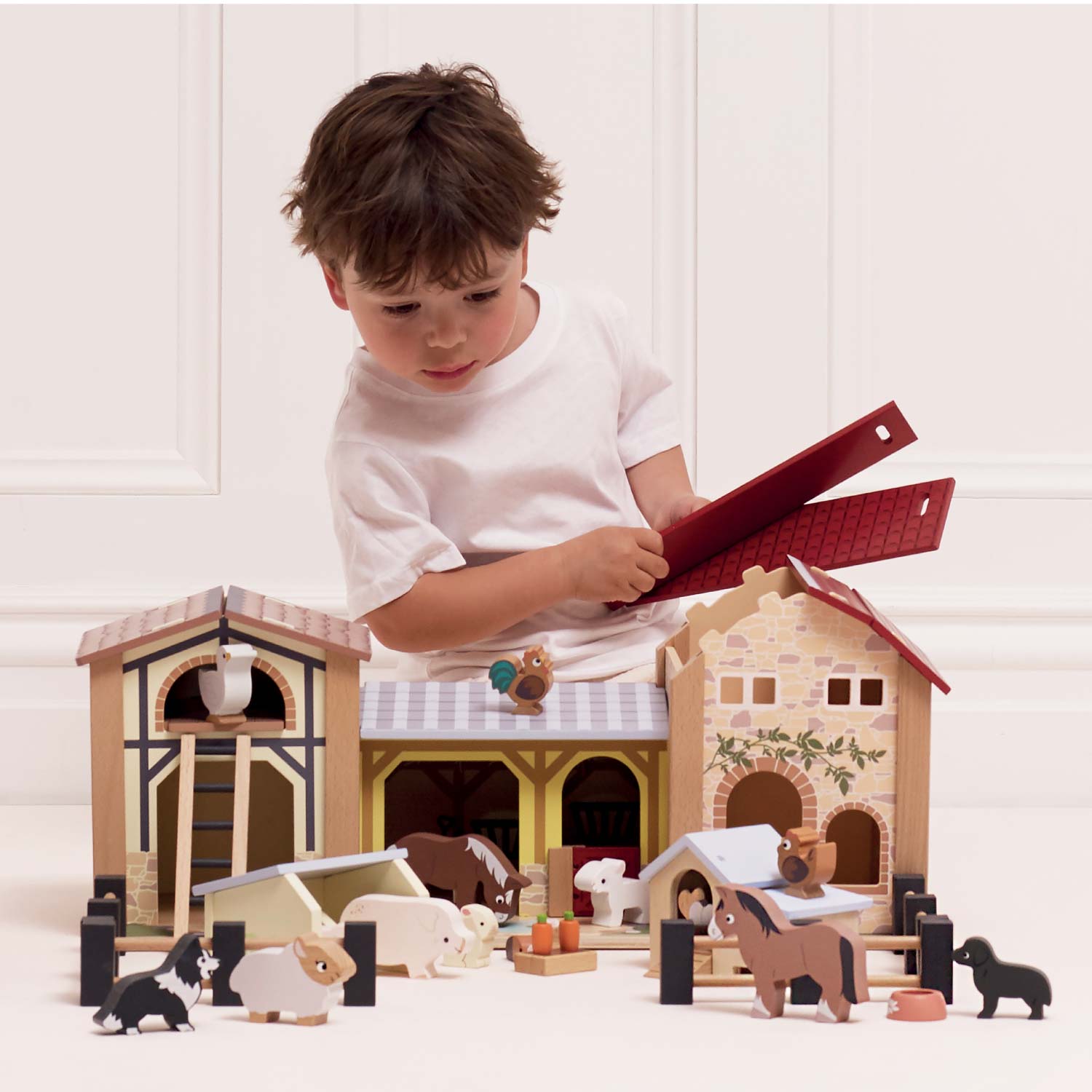 Child playing with a wooden toy farm set on a white surface.