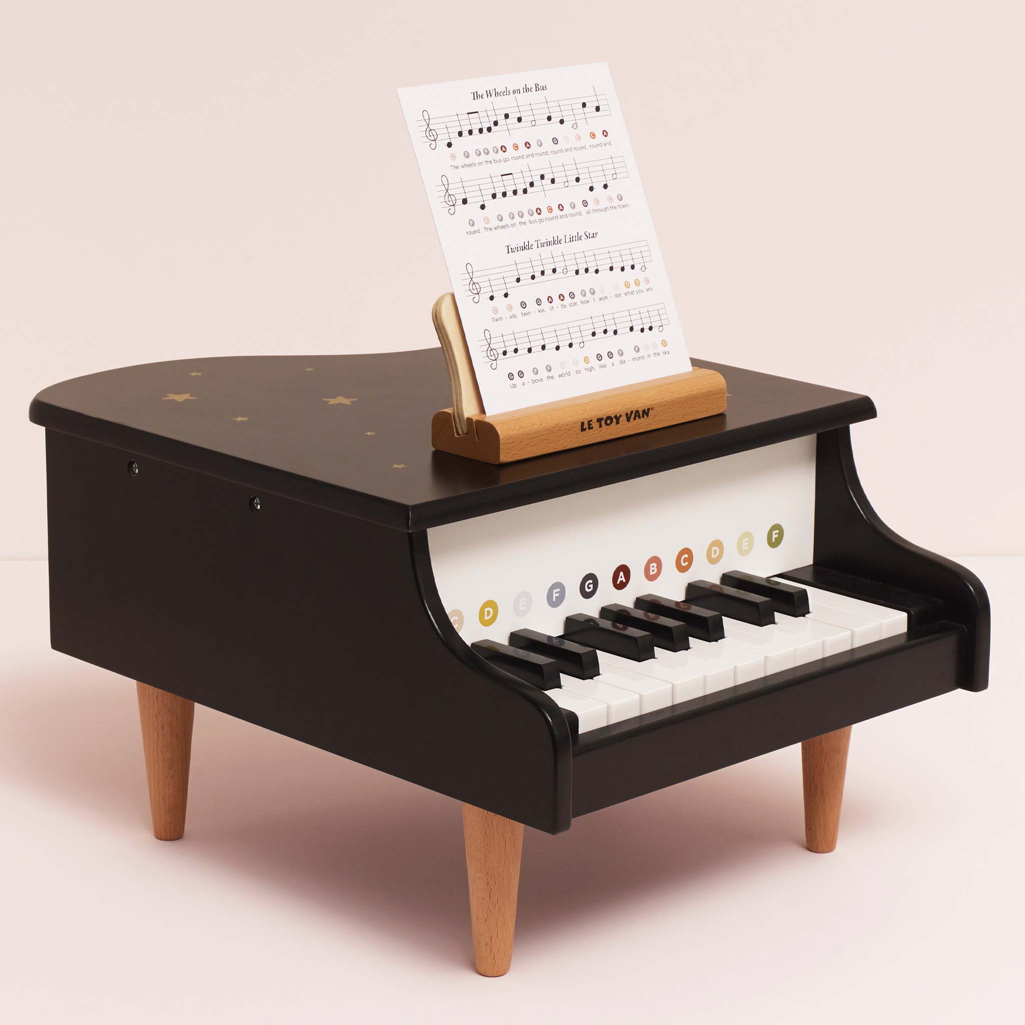 Black toy piano with wooden legs on a light pink background