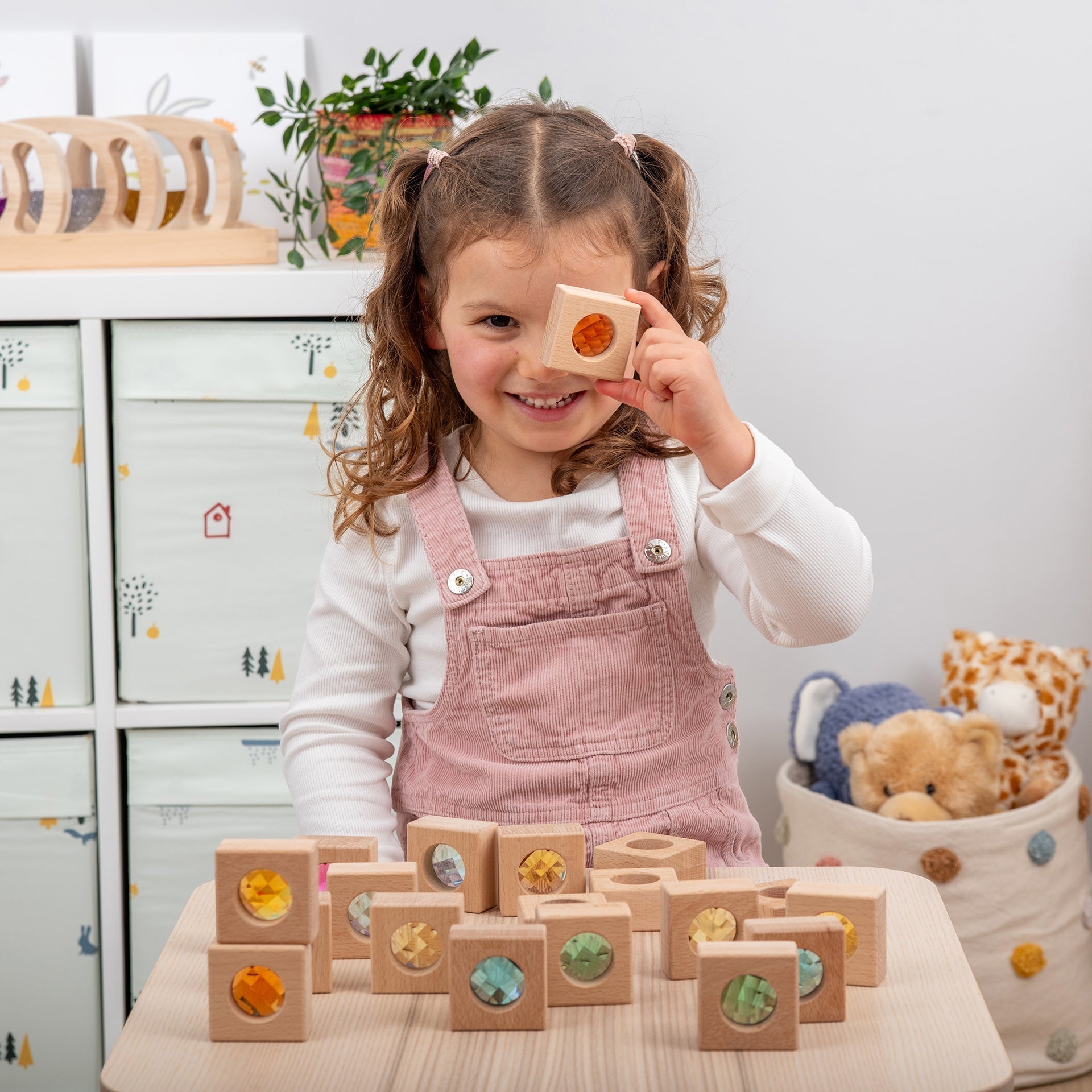 Child playing with wooden blocks in a room with toys and furniture.