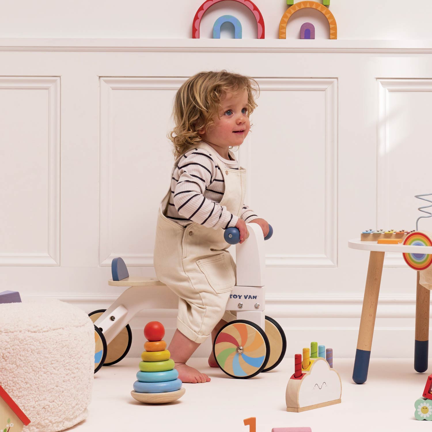Child playing with colorful toys in a room with white walls and wooden furniture.