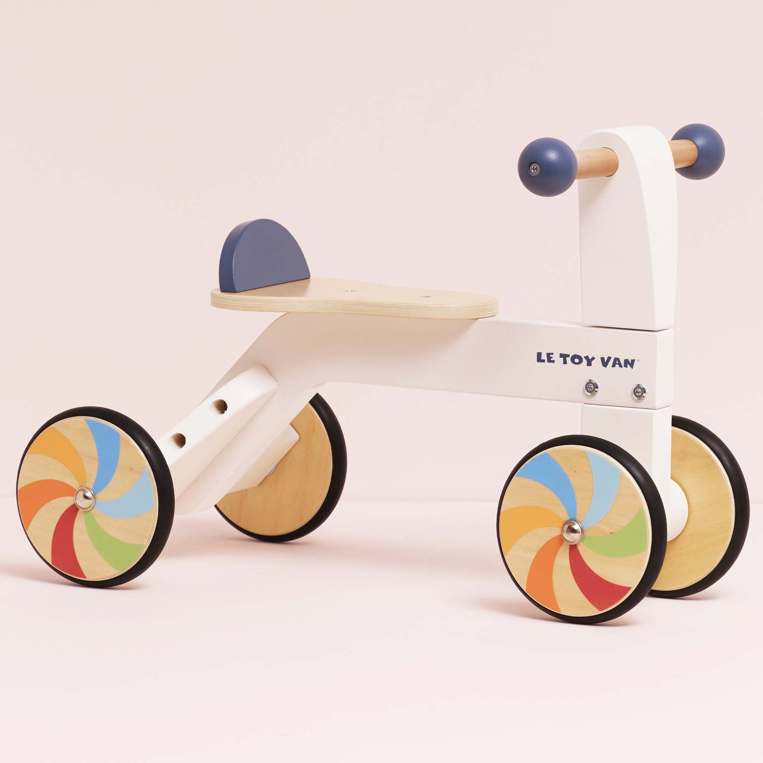 Children's balance bike with colorful wheels on a light pink background, featuring the Le Toy Van brand.
