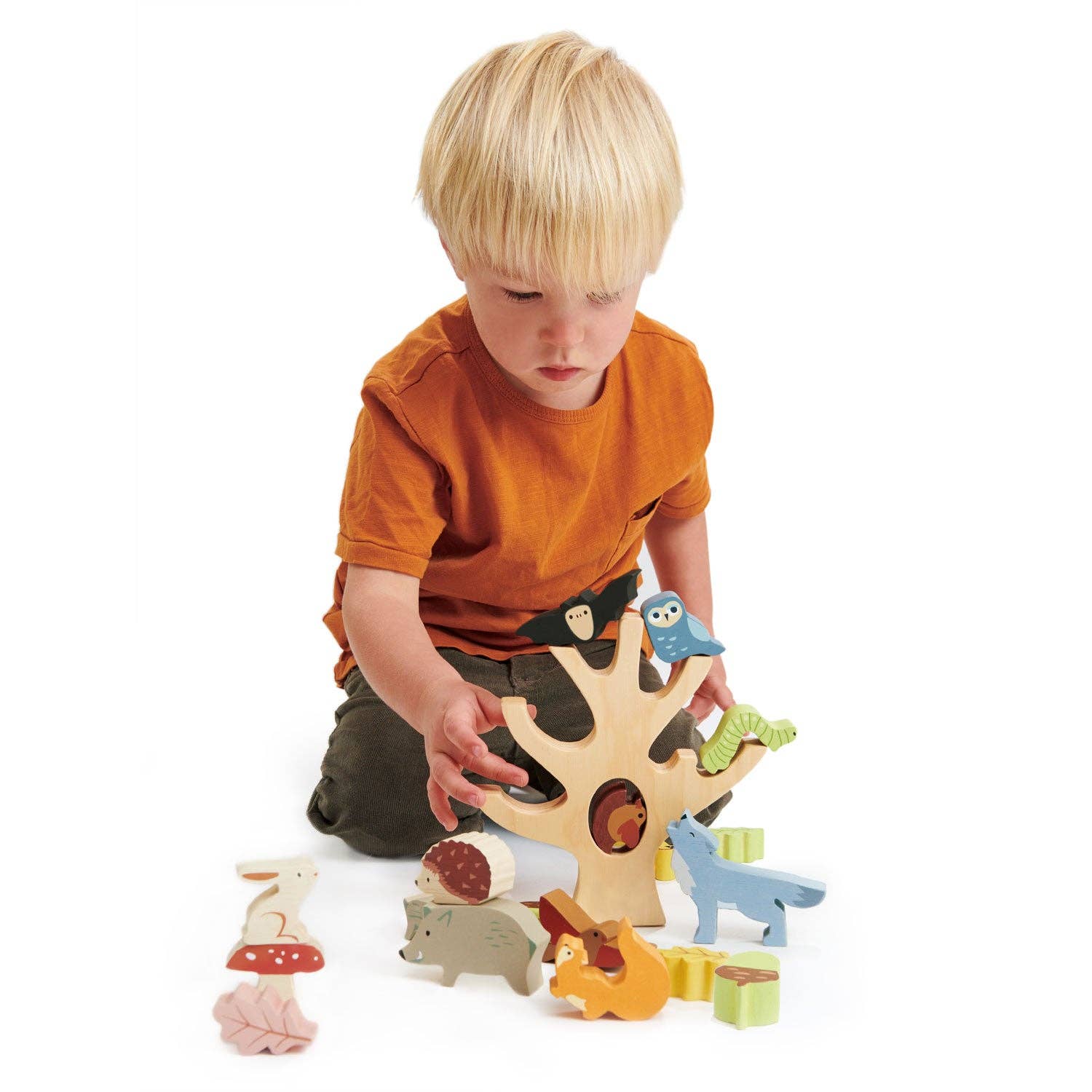 Child playing with a wooden tree set with animal figures on a white background
