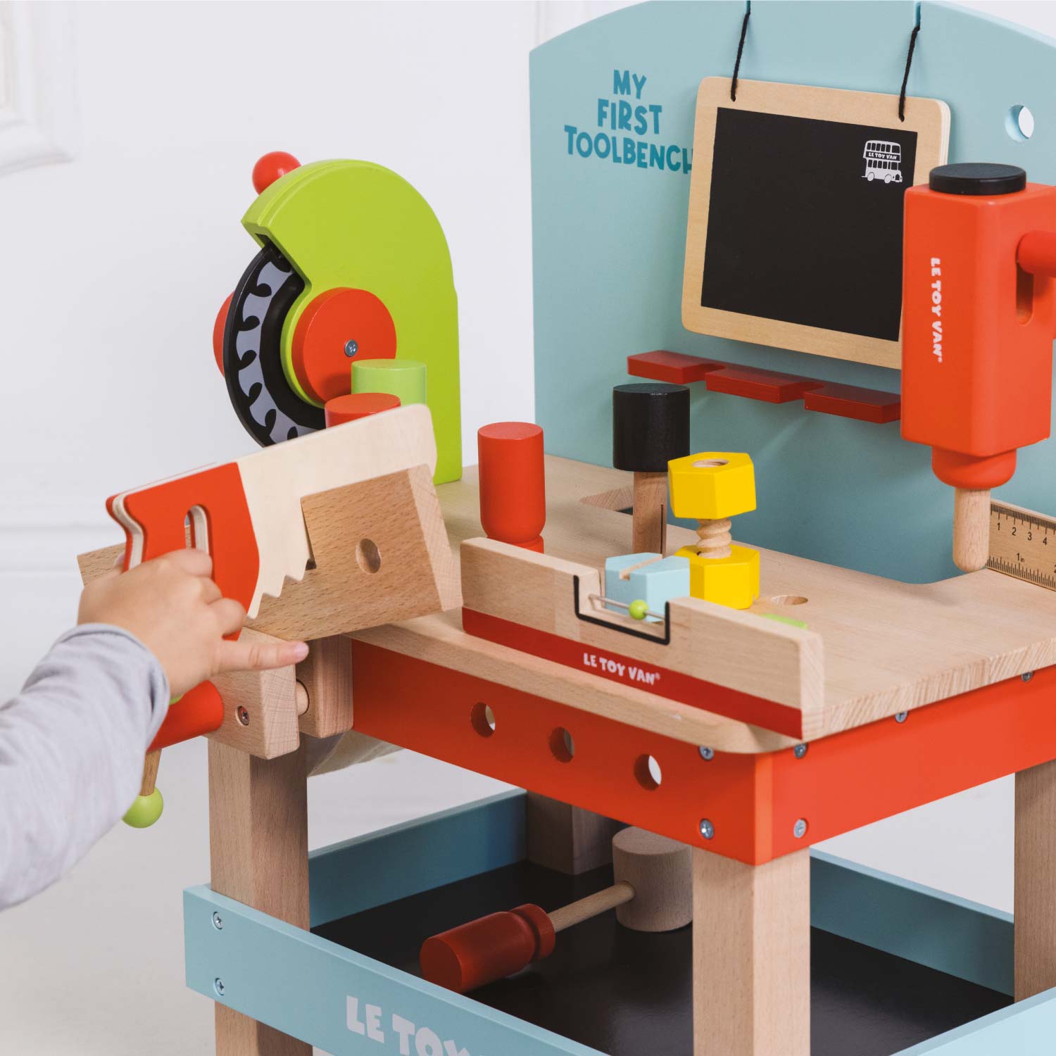 Children's toy workbench with various tools and a hand interacting with it, set against a light blue background.