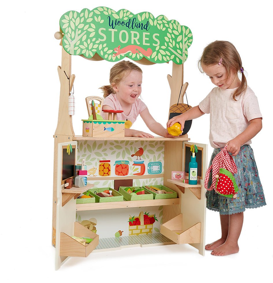 Children playing with a wooden toy store set up with various items on a white background