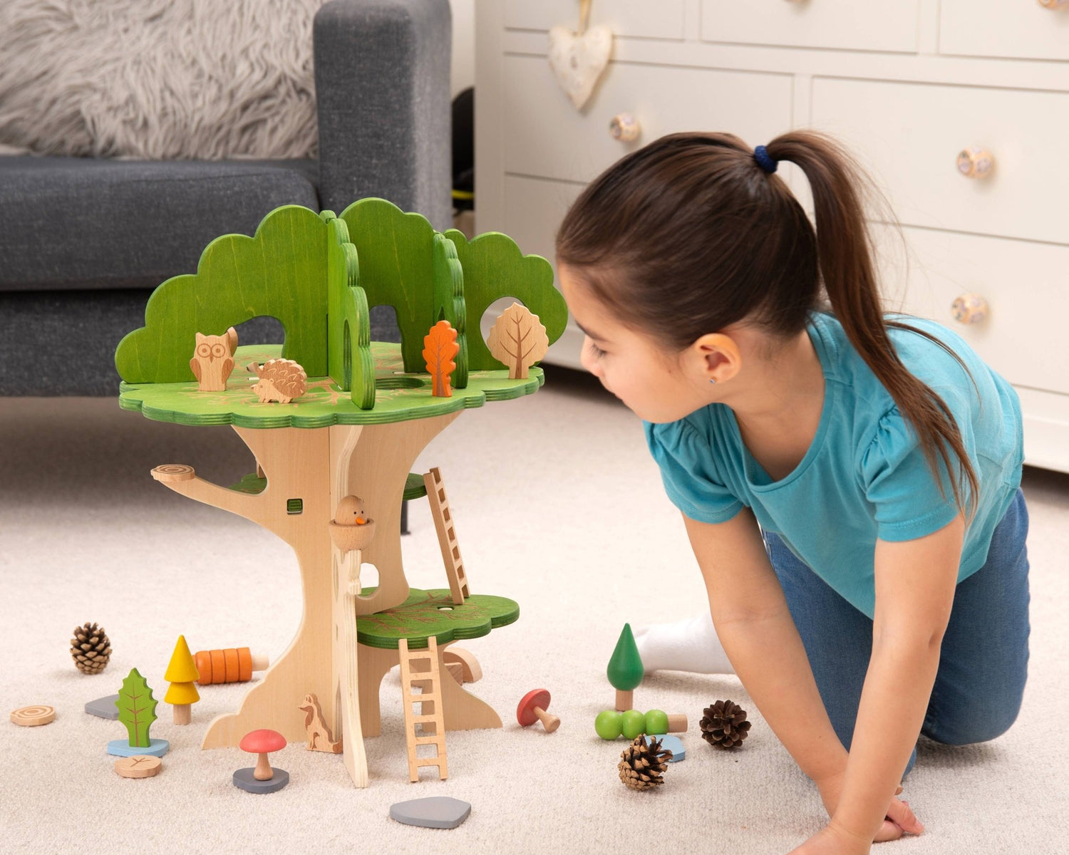 Child playing with a wooden treehouse toy set on a carpeted floor.