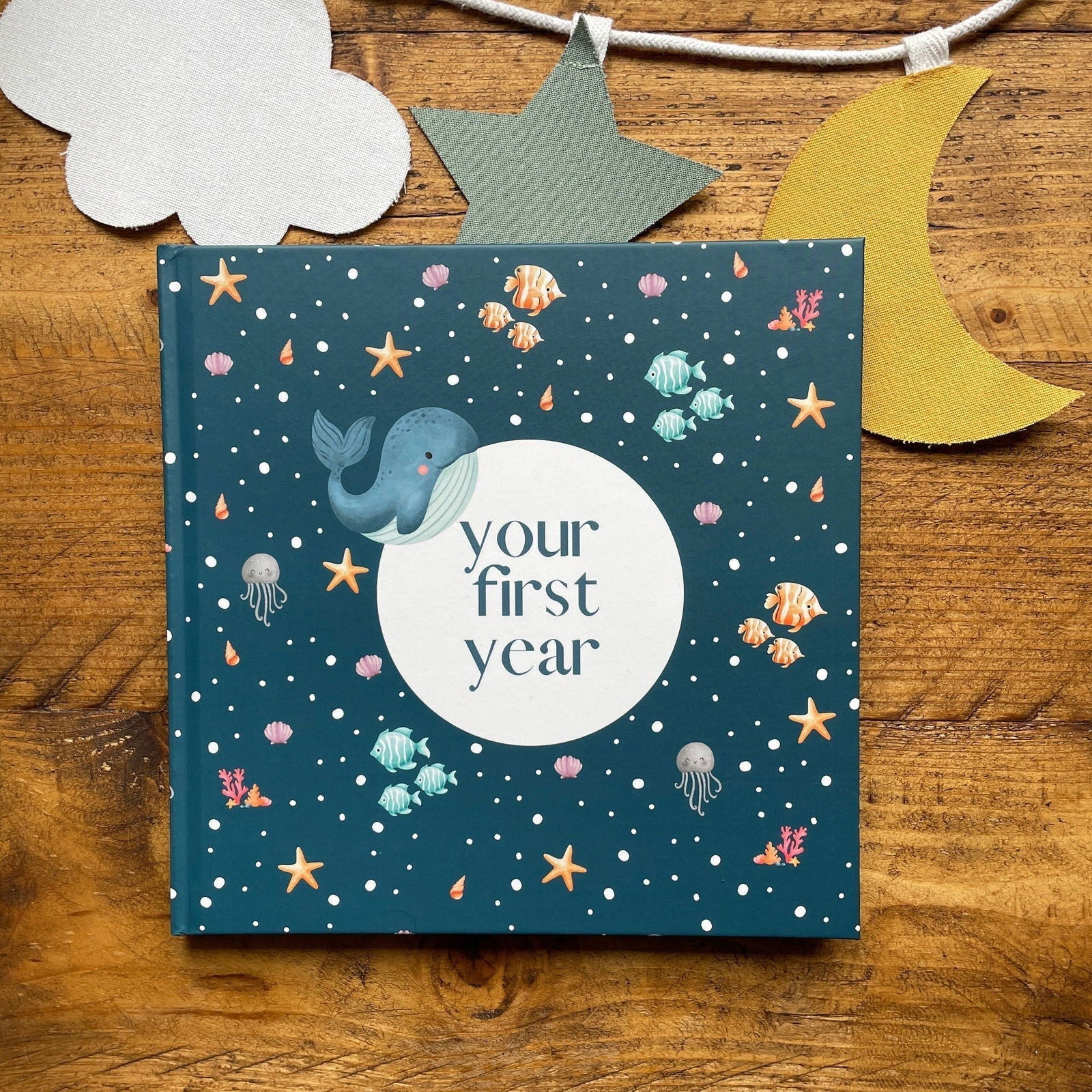 Book titled 'Your First Year' with a whale illustration on a wooden surface with decorative elements.