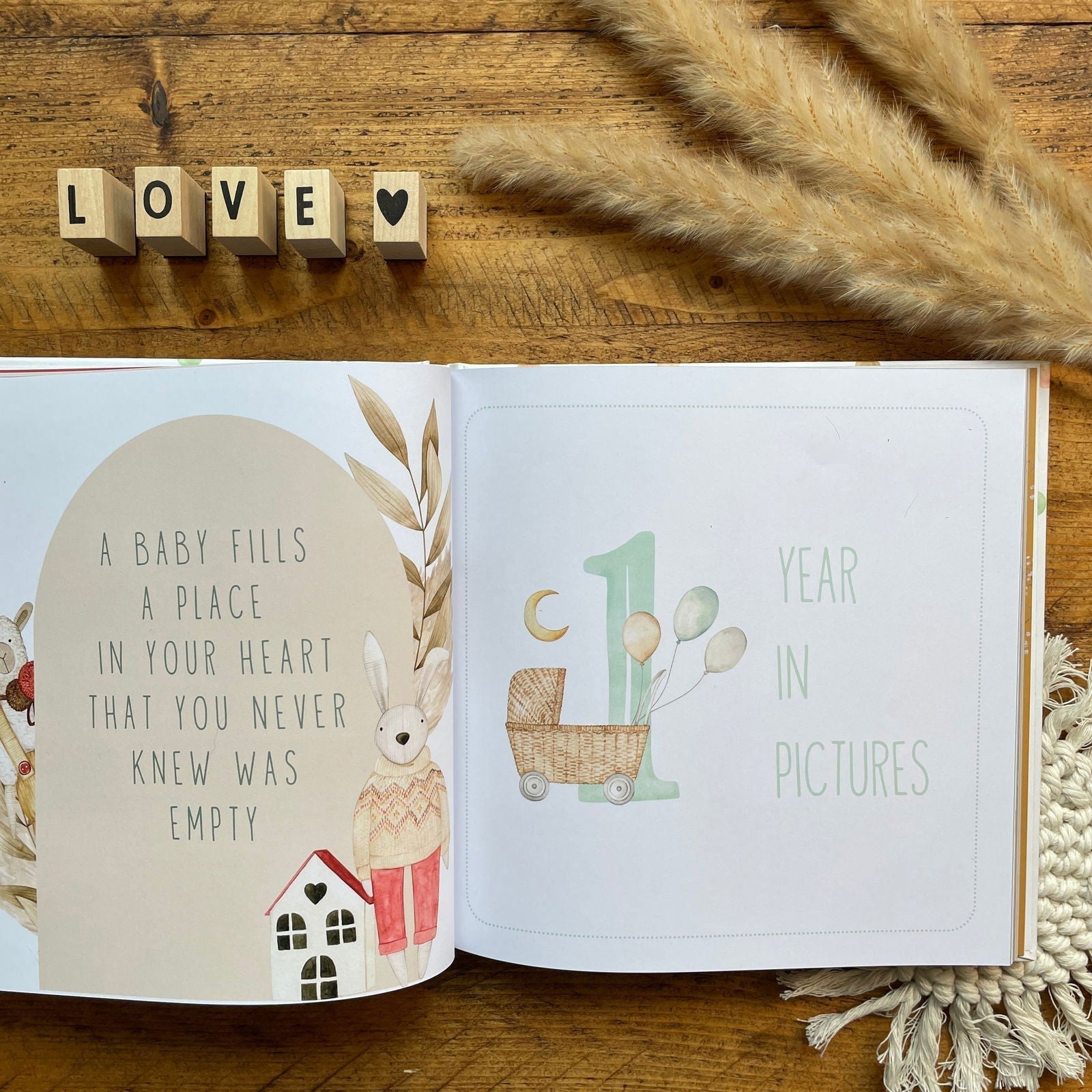 Open book with baby-themed illustrations and 'LOVE' spelled out with wooden blocks on a wooden surface.